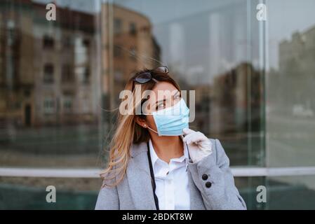 Primo piano di giovane bella donna d'affari caucasica bionda con maschera di fronte all'azienda. Foto Stock