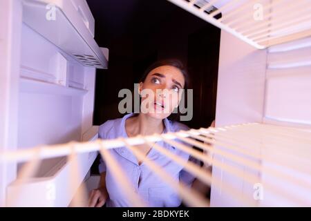 Giovane donna che guarda le mensole vuote del suo frigorifero Foto Stock