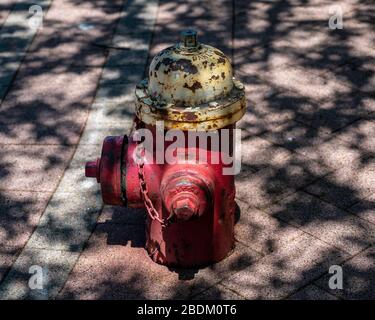 Un solone ruggine rosso e giallo fuoco idrante, marciapiedi pavers in luce del sole e ombra da un albero preso nel centro di Hartford Foto Stock