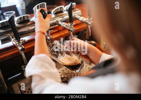 Una giovane cameriera bionda e attraente caucasica che versa birra in un bar Foto Stock