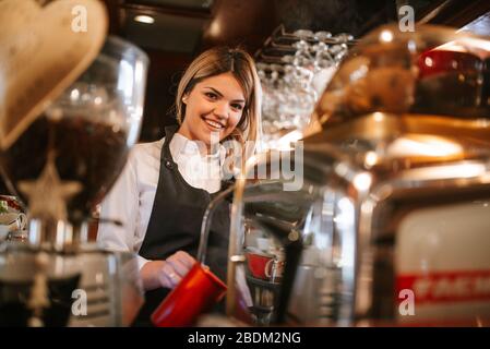 Una giovane e attraente cameriera bionda caucasica fa il caffè in un caffè Foto Stock