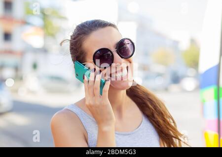 Donna euforica che parla con il suo smartphone in una stazione degli autobus mentre è in attesa Foto Stock
