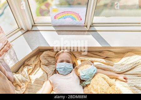 Bambino con il giocattolo dell'orso del teddy in maschere mediche durante la quarantena di Covid-19 nel paese. Rimani a casa Campagna sui social media per la prevenzione del coronavirus, andiamo tutto Foto Stock