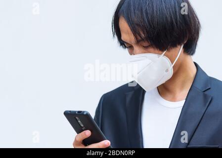 Un uomo asiatico indossa la maschera N95 e usa lo smartphone Foto Stock