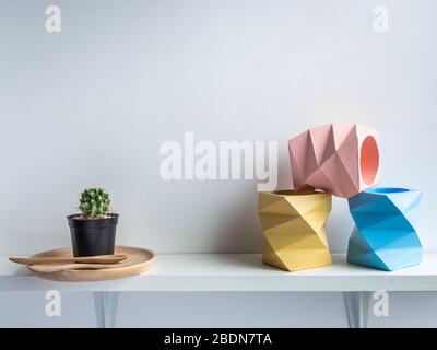 Vaso Cactus. Pentola di calcestruzzo. Tre piantatrici geometriche vuote blu, rosa e giallo e cactus verde su piatto di legno su ripiano di legno bianco i Foto Stock