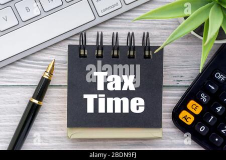 TAX TIME testo con fiore decorativo, calcolatrice, penna stilografica, tastiera e blocco note su sfondo in legno. Concetto di business e comunicazione Foto Stock