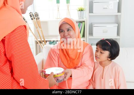 Donna che dà i biscotti più anziani durante Hari Raya. Stile di vita familiare malese o malese a casa. Foto Stock