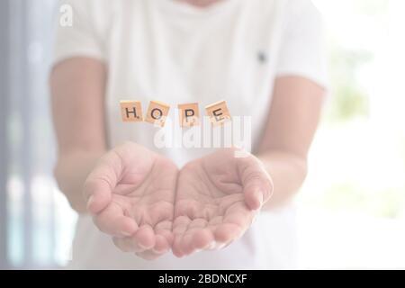 Pezzi Scrabble che formano la parola speranza sulle mani - fuoco selettivo. Foto Stock