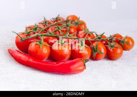 Primo piano con rametti di pomodori ciliegini maturi e cialda di peperoncino rosso dolce. Tasto alto Foto Stock