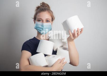 Giovane donna caucasica in maschera protettiva che tiene molti rotoli di carta igienica. Panico, acquisto per la quarantena coronavirus Foto Stock