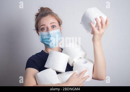 Giovane donna caucasica in maschera protettiva che tiene molti rotoli di carta igienica. Panico, acquisto per la quarantena coronavirus Foto Stock