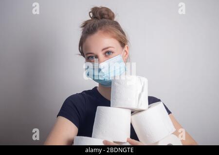 Giovane donna caucasica in maschera protettiva che tiene molti rotoli di carta igienica. Panico, acquisto per la quarantena coronavirus Foto Stock