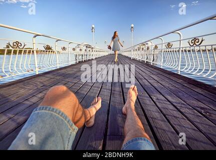 Donna in abito a righe con Red Hat andando per il suo ragazzo da sul molo in spiaggia Foto Stock