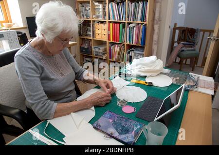 Donna anziana che fa i cappelli dei dispositivi di protezione personale (PPE) per il NHS nella crisi di Covid-19 Foto Stock