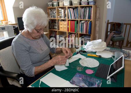 Donna anziana che fa i cappelli dei dispositivi di protezione personale (PPE) per il NHS nella crisi di Covid-19 Foto Stock