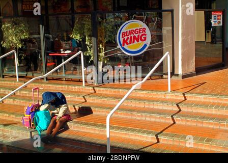 Los Angeles, CA, USA - 22 marzo 2005: Donna senzatetto non identificata con i suoi bagagli sui gradini davanti ad un ristorante Foto Stock