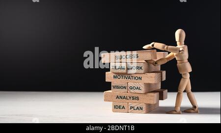 Uomo di legno costruisce la torre di mattoni lunghi di legno con le parole. Costruire il vostro futuro di successo. Concetto di successo, lavoro di squadra, motivazione, obiettivo di visione, un Foto Stock