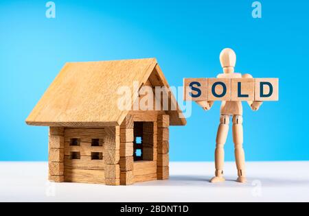 Figura di uomo di legno tenere cubetti con testo blu venduto. Immobile in vendita. Mini casa in legno. Concetto di vendita di una casa, appartamento, immobiliare. Mercato di Foto Stock