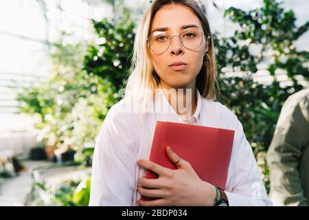 Giovane ingegnere agricolo che lavora in serra. Giovane scienziata femminile che guarda la macchina fotografica Foto Stock