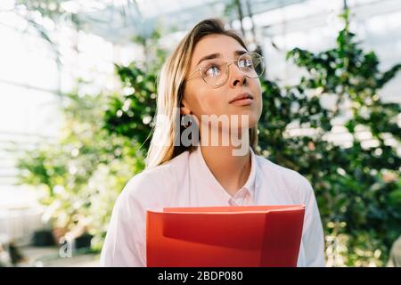 Giovane ingegnere agricolo che lavora in serra. Giovane scienziata femminile guarda via Foto Stock