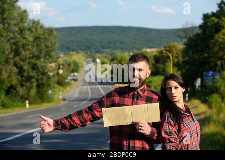 Coppia in amore viaggiando da hitchhiking, spazio copia. Uomo e donna cercano di fermare l'auto con il cartello di cartone, pollici in su. Avventura e hitchhiking concetto. Coppia con i volti pensivi viaggiano con arresto automatico. Foto Stock