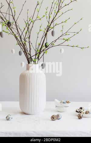 Albero di Pasqua e uova di quaglia su un tavolo bianco. Rami di betulla decorati con uova dipinte di bianco e grigio. Moderno decor minimalista di Pasqua Foto Stock