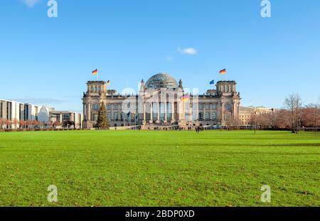 Berlino, Germania - 9 dicembre 2019: Vista del palazzo del Reichstag con bandiera tedesca sul vento dal campo di erba verde Foto Stock