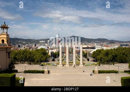 Vista di persone che camminano in una piazza chiamata 'Placa de les Cascades'. I luoghi di vista sono 'font Magica de Montjuic' e la città di Barcellona. È un'estate soleggiata Foto Stock