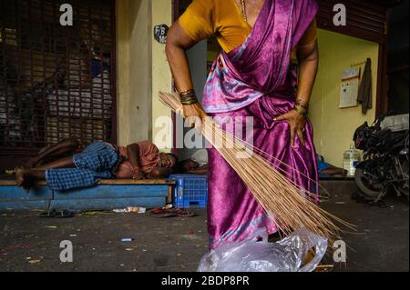 Donna indiana che si sta spazzando come gli uomini in sottofondo dormire, mercato di Koyambedu, Chennai, India Foto Stock