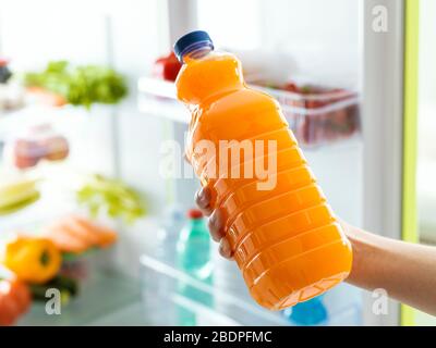 Donna che prende una bottiglia di succo d'arancia fresco dal frigo, concetto di bevanda sana Foto Stock