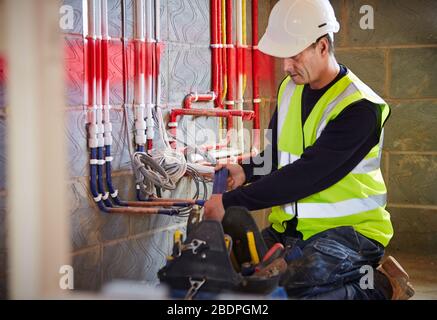 Elettricista al lavoro che installa il tubo per passare i cavi elettrici nel cantiere Foto Stock
