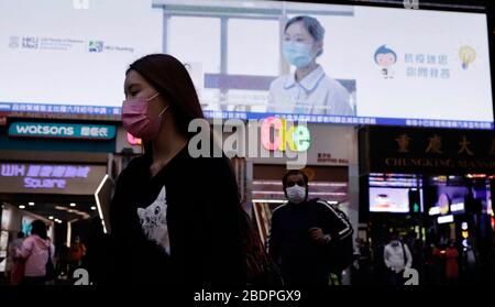 Hong Kong, CINA. 9 Aprile 2020. Donna mascherata passeggiata attraverso il centro urbano nel quartiere commerciale, dietro di lei vedere un'immagine di infermiere mascherato che spiega la misura precauzionale contro le infezioni da coronavirus.April-9, 2020 Hong Kong.ZUMA/Liau Chung-ren Credit: Liau Chung-ren/ZUMA Wire/Alamy Live News Foto Stock