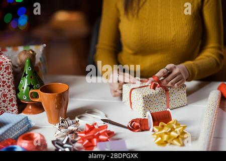 Donna che avvolge i regali di Natale a casa, sta legando un arco del nastro: Le feste e le celebrazioni concetto Foto Stock