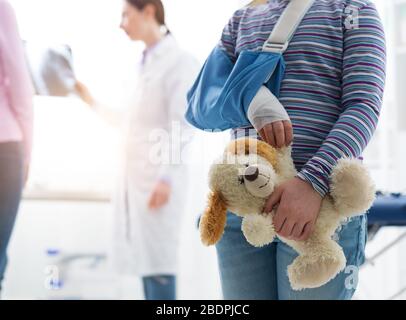 Ragazza carina con braccio di sostegno nell'ufficio del medico, lei sta tenendo un orso peloso plushie, bambini e concetto di salute Foto Stock