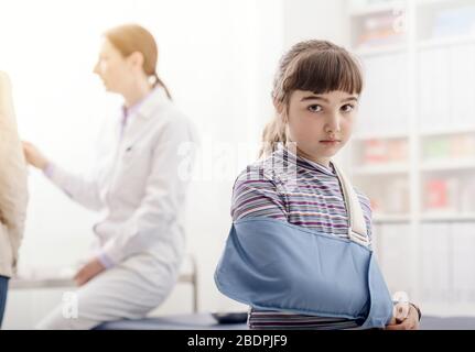 Ragazza con braccio rotto nell'ufficio del medico, sta portando un braccio e guardando la macchina fotografica Foto Stock