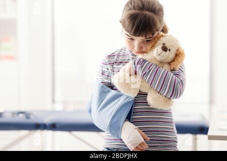 Ragazza carina nell'ufficio del medico che aspetta di essere visitata, lei sta tenendo il suo orso di teddy Foto Stock