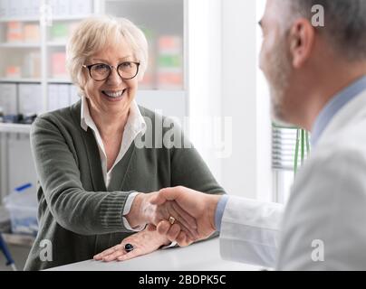 Dottore che accoglie una paziente sorridente di sesso femminile nel suo ufficio e che scuote la mano Foto Stock