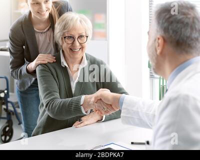 Dottore che accoglie una paziente sorridente di sesso femminile nel suo ufficio e che scuote la mano Foto Stock