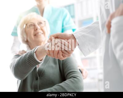 Medico che dà una stretta di mano ad una paziente e ad un'infermiera di cura, di salute e di fiducia sorridenti Foto Stock