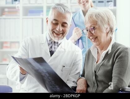 Radiologo professionista che esamina un'immagine a raggi X con un paziente senior durante una visita in clinica, il medico punta e fornisce consigli Foto Stock