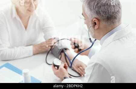 Medico professionista che misura la pressione sanguigna di una paziente di sesso femminile senior durante una visita, ipertensione e prevenzione Foto Stock