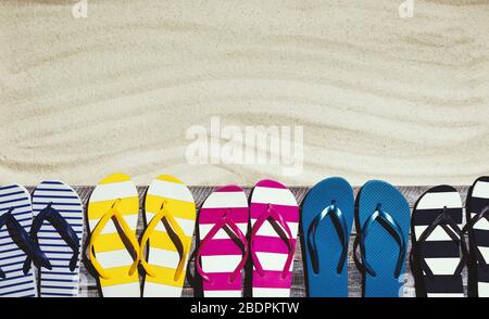 Set di infradito colorate sul ponte della spiaggia e di sabbia tropicale pulita, concetti estivi e di vacanza, spazio copia vuoto Foto Stock