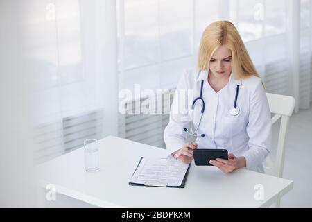 Medico caucasico femmina che usa la compressa e la diagnosi di scrittura nei documenti di forma medica Foto Stock