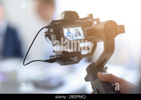 Videomaker professionale che scatta un video, attori disfocillati in background, concetto di video e comunicazione Foto Stock