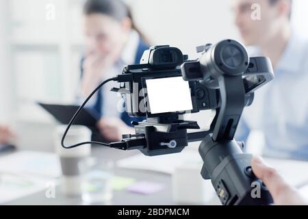 Videomaker professionale che scatta un video, attori disfocillati in background, concetto di video e comunicazione Foto Stock