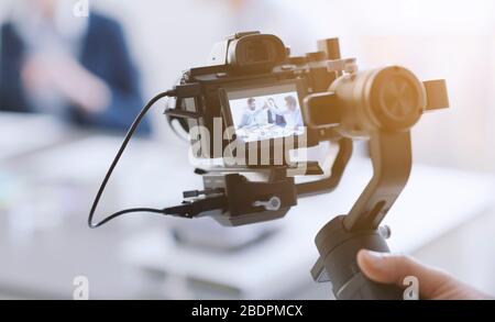Videomaker professionale che scatta un video, attori disfocillati in background, concetto di video e comunicazione Foto Stock