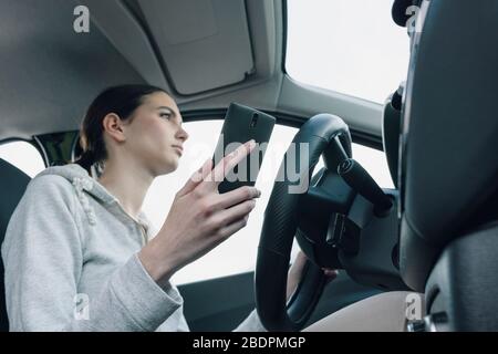 Giovane donna distratta e incurante che usa il suo smartphone durante la guida, concetto di sicurezza di guida Foto Stock