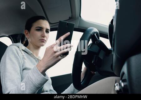 Giovane donna distratta e incurante che usa il suo smartphone durante la guida, concetto di sicurezza di guida Foto Stock