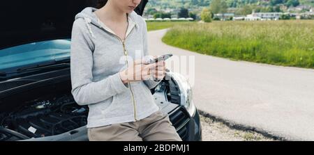 Giovane donna triste che chiama un servizio di riparazione auto con il suo telefono, sta avendo un guasto auto in una strada di campagna Foto Stock