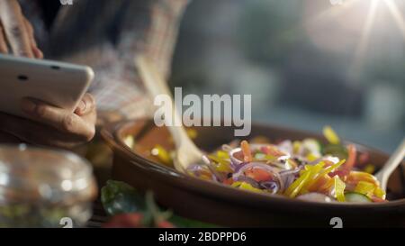 Donna alla ricerca di ricette sane online sulla sua tavoletta digitale e la cottura di verdure fresche miste in una pentola di argilla Foto Stock